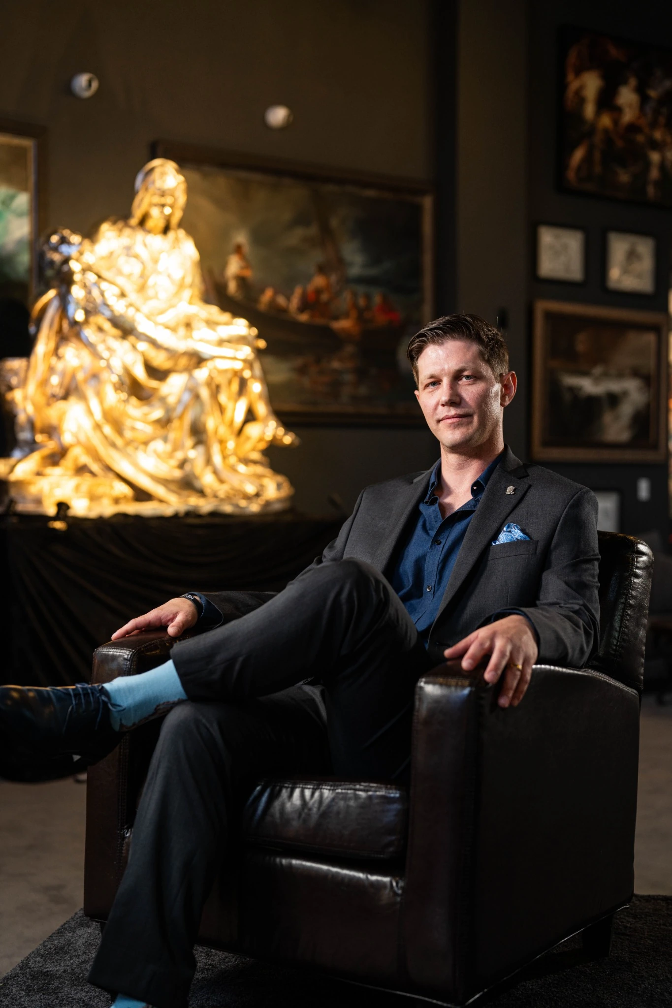 Seated portrait in a dark gallery beside an illuminated sculpture